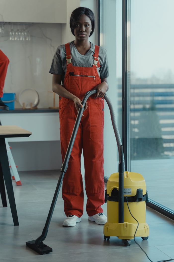 Une femme adulte en combinaison rouge utilise un aspirateur dans un intérieur moderne, concentrée sur les tâches de nettoyage.